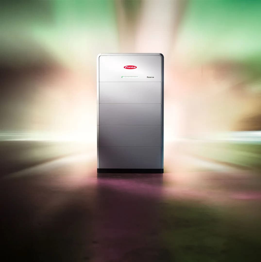 Fronius Reserva batteri set forfra i et mørkt rum, belyst bagfra af grønt og rosa lys